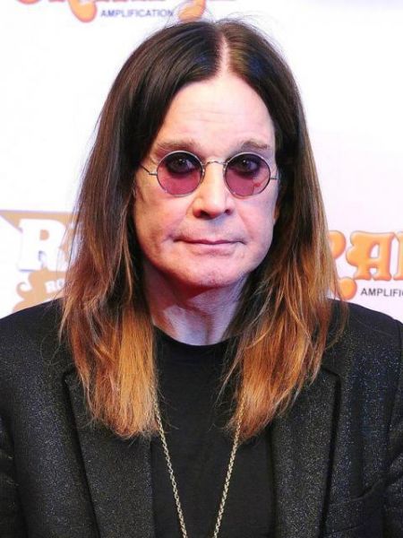 ozzy wearing a black coat, shoulder lenth dyed hair and round glasses 